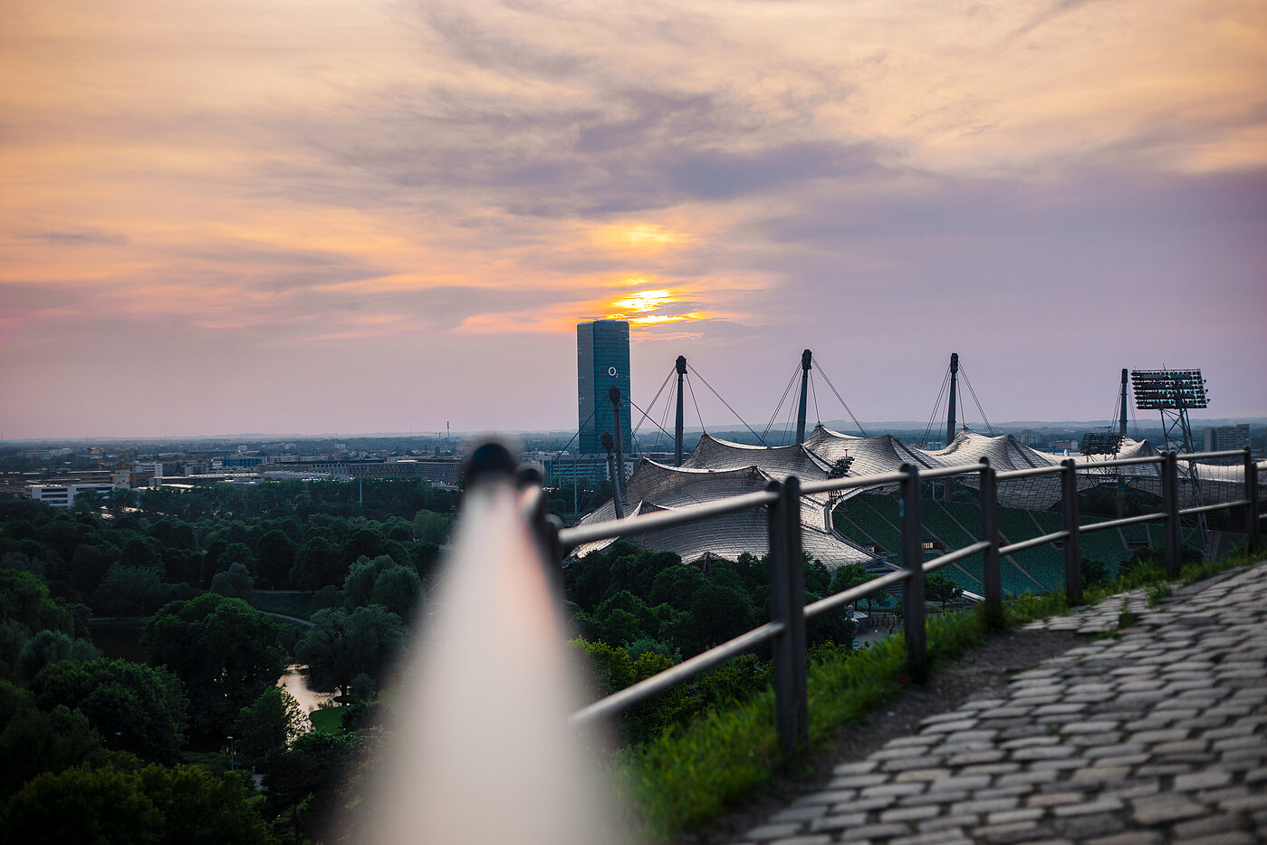 Olympiapark Zu sehen ist eine Brüstung, im Hintergrund ist das Zeltdach der Olympiahalle bei Sonnenuntergang